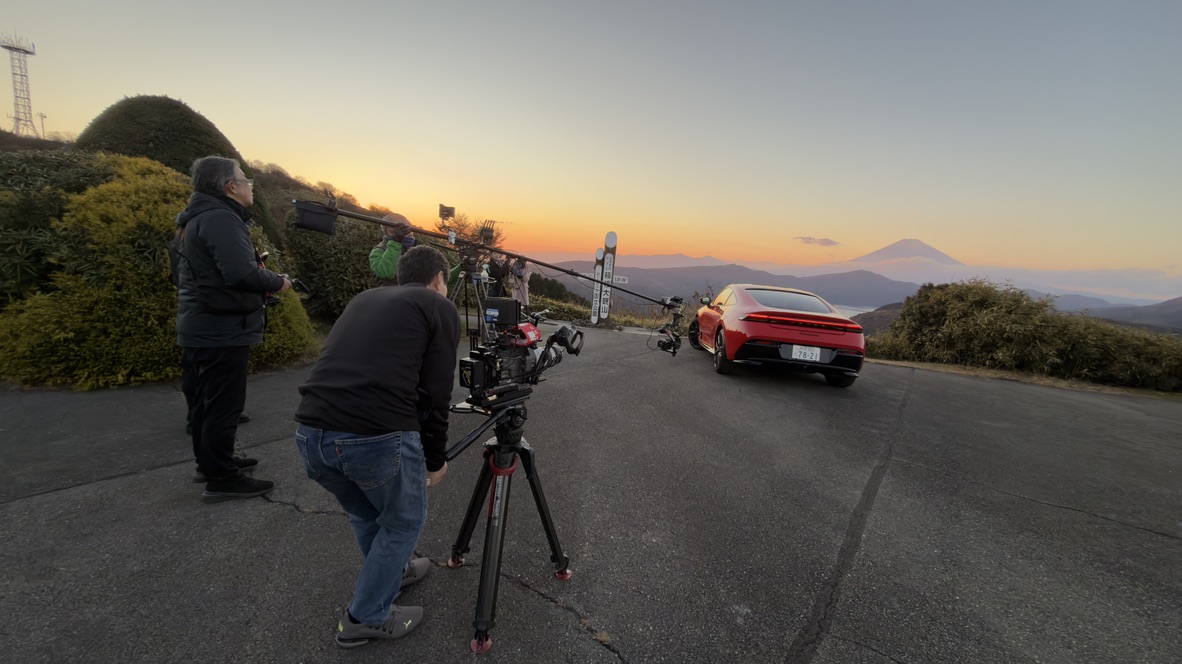 夕景の中で赤い車両を撮影するスタッフとカメラ