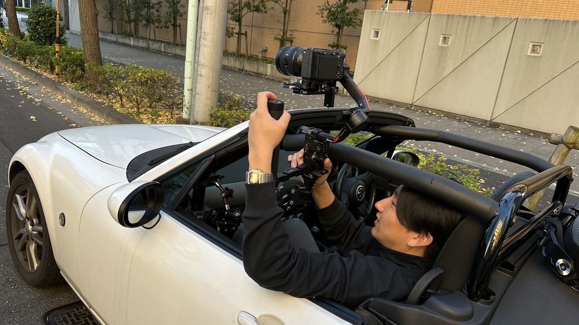 オープンカーの車内でジンバル付きカメラを構えるスタッフ