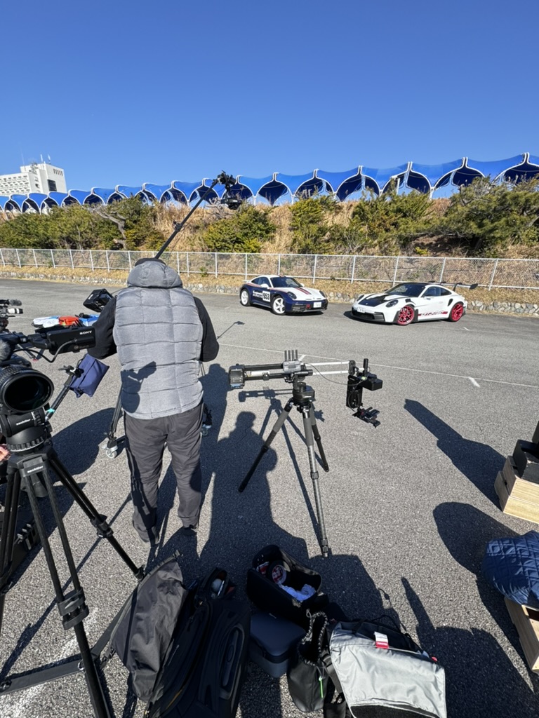 白いスポーツカー2台とクレーンやカメラを準備する撮影スタッフ