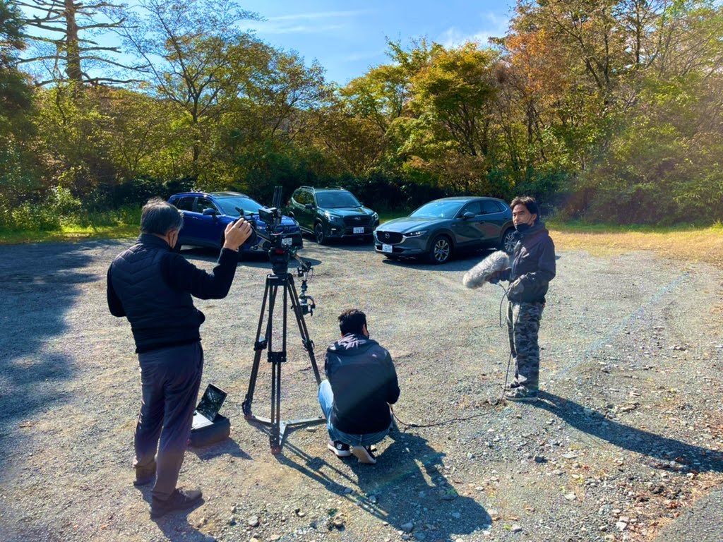 屋外に並ぶ車両とカメラやマイクを準備するスタッフ